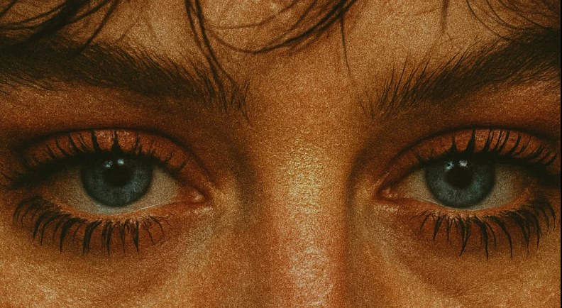 Close-up of grey-blue eyes on a warm amber-toned face with heavy film grain