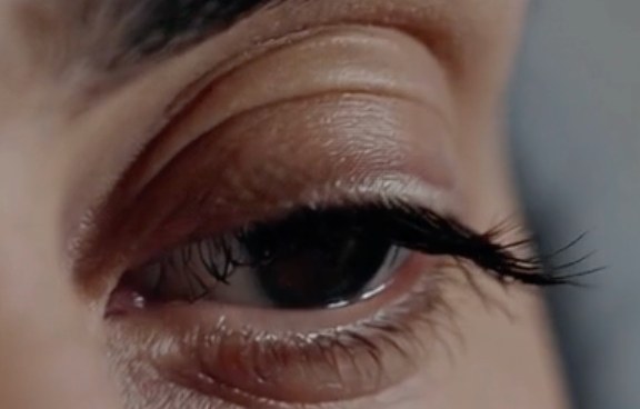 Extreme close-up of a single eye with dark lashes, half-lidded and watchful, in soft focus