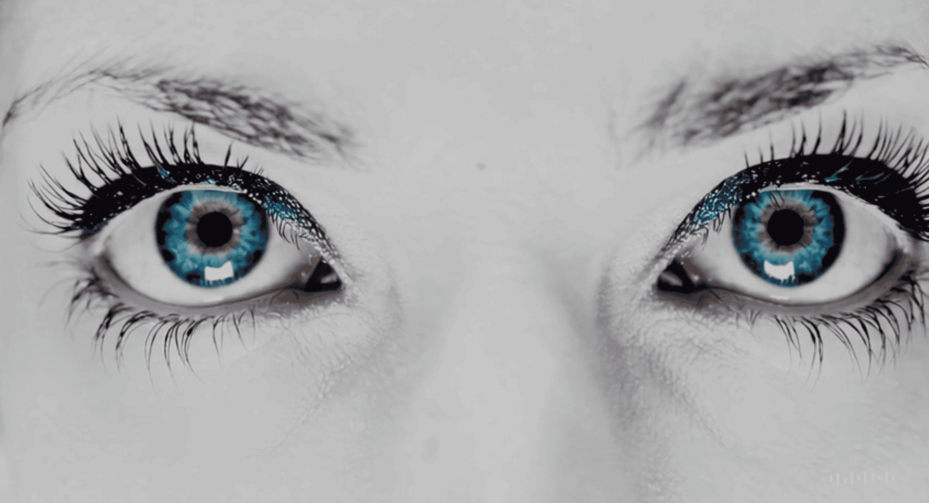 Close-up of wide blue eyes against a bleached monochrome face, staring directly at the viewer